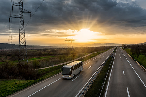 A charter bus drives on an empty highway at sunset