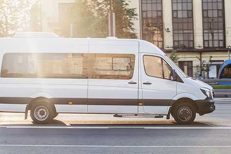 A white minibus drives on a city street